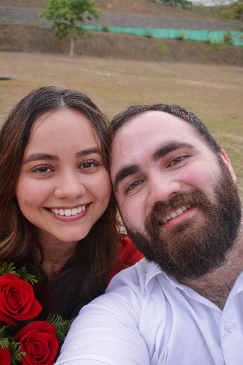 Luana e Emerson sentados na grama com o buquê